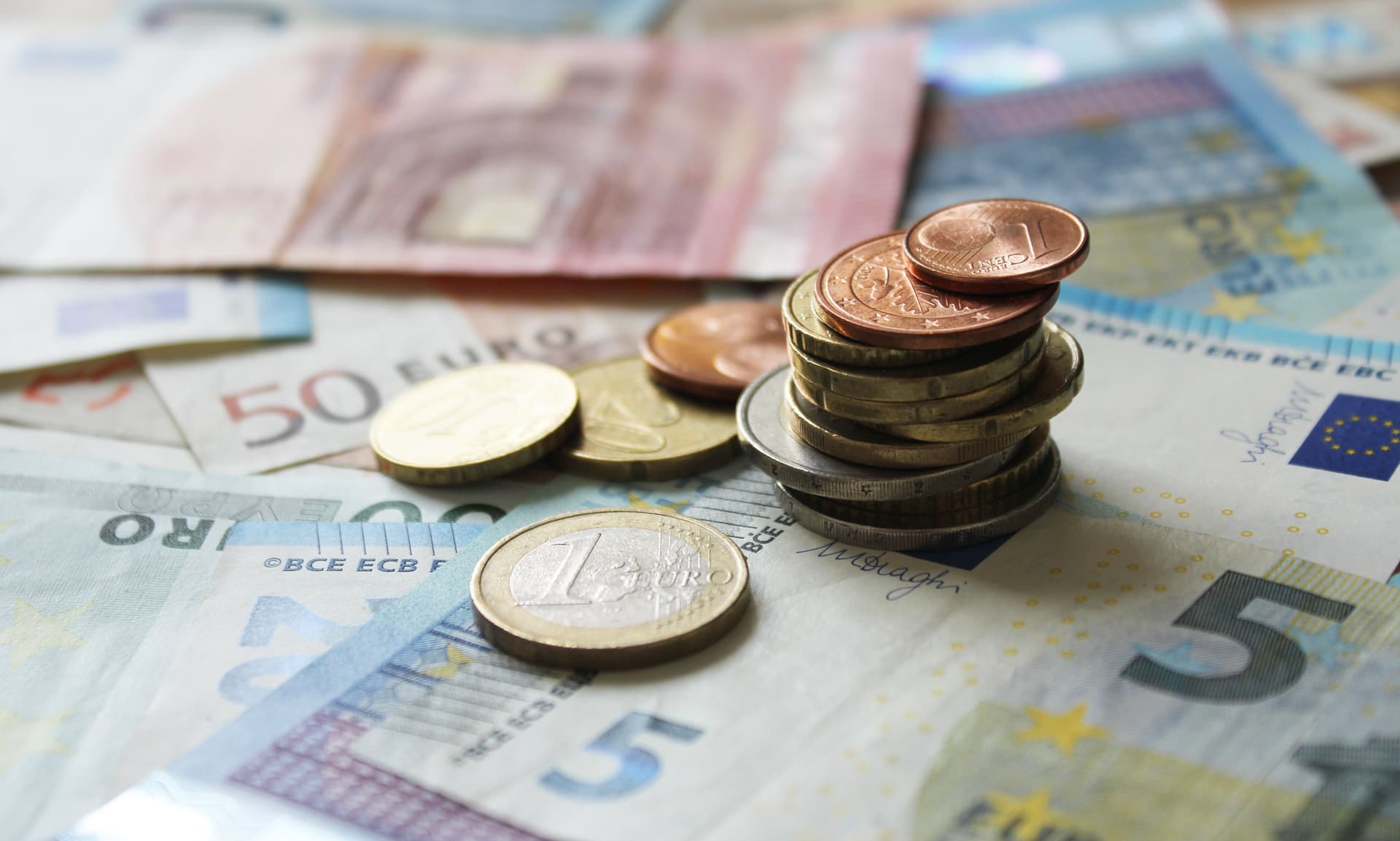 Gestapelte Euro-Münzen auf Geldscheinen, im Fokus eine Ein-Euro-Münze